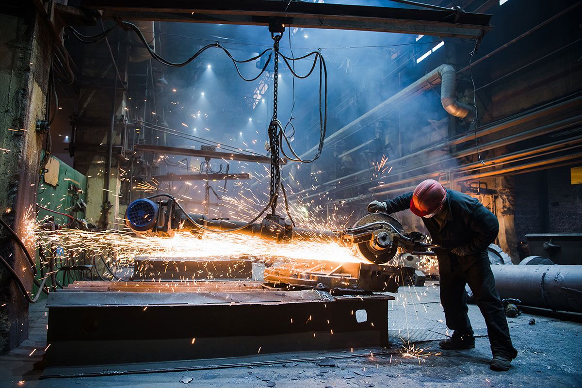 Arbeiter bei der Metallverarbeitung mit einem Winkelschleifer in einer Werkshalle.