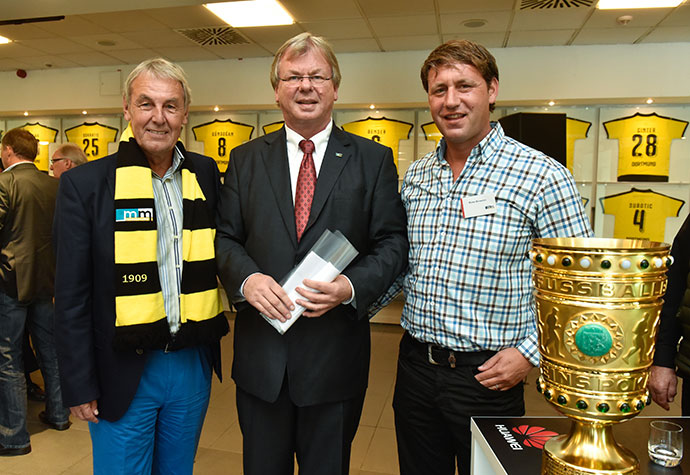 Fernsehmoderator und Sportreporter Jörg Wontorra, m+m Geschäftsführer Michael Müller und Zeljko Buvac stehen neben dem DEF-Pokal. 